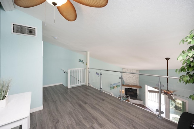 unfurnished living room featuring a fireplace, vaulted ceiling, wood finished floors, and visible vents