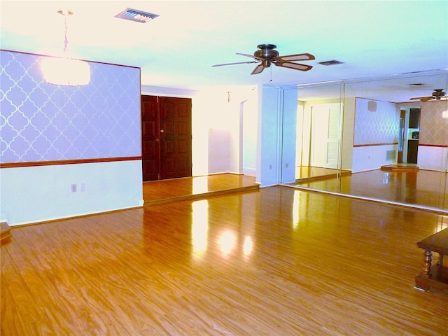 unfurnished room featuring visible vents, a ceiling fan, wood finished floors, wallpapered walls, and baseboards