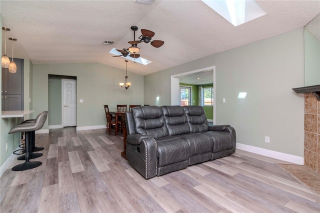 living room with lofted ceiling with skylight, wood finished floors, visible vents, and a textured ceiling