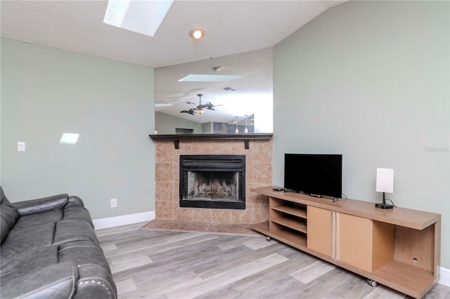 living area with baseboards, lofted ceiling with skylight, light wood-type flooring, a tile fireplace, and a textured ceiling