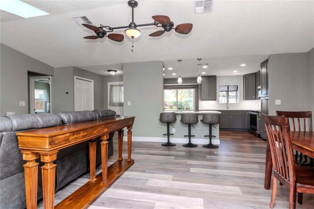 living area with wood finished floors, visible vents, baseboards, a skylight, and a textured ceiling