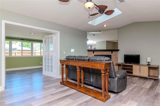 interior space featuring a ceiling fan, wood finished floors, baseboards, a fireplace, and lofted ceiling with skylight