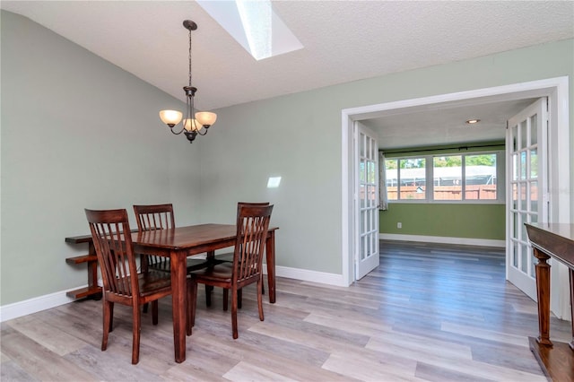 dining room featuring baseboards, a chandelier, lofted ceiling with skylight, wood finished floors, and a textured ceiling