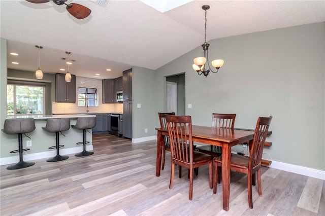 dining area with lofted ceiling, light wood-style floors, baseboards, and a textured ceiling