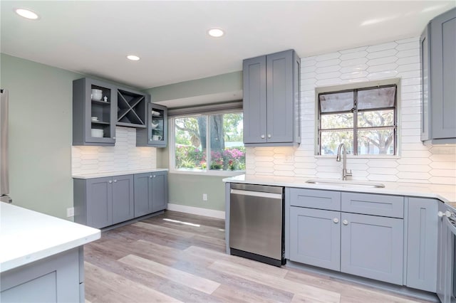 kitchen featuring gray cabinets, a sink, stainless steel dishwasher, light wood-style floors, and glass insert cabinets