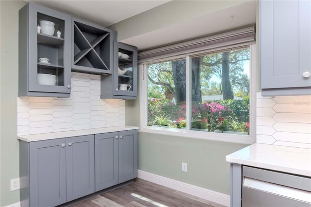 kitchen featuring gray cabinetry, glass insert cabinets, baseboards, light countertops, and decorative backsplash