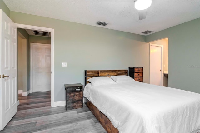 bedroom featuring visible vents, a textured ceiling, baseboards, and wood finished floors