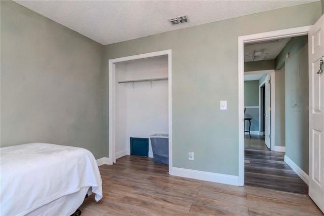 bedroom featuring visible vents, baseboards, a textured ceiling, and wood finished floors