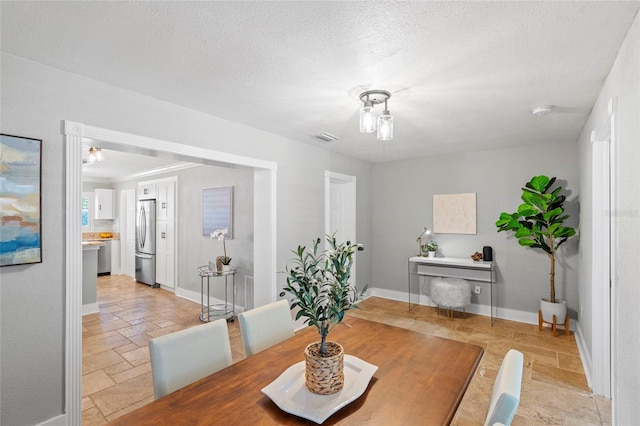 dining space featuring stone tile flooring, visible vents, a textured ceiling, and baseboards