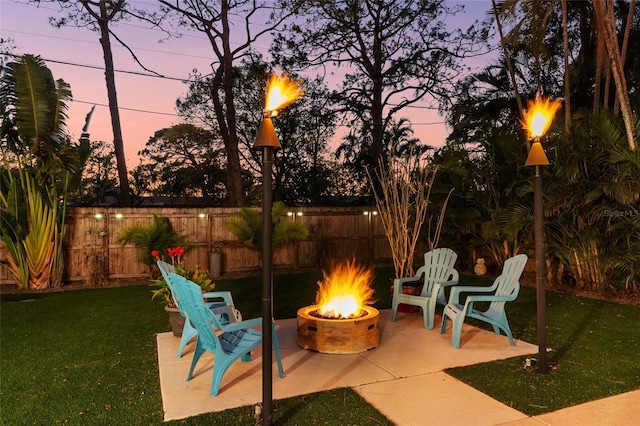 patio terrace at dusk featuring a yard, a fire pit, and fence