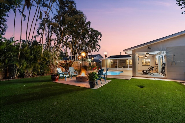 yard at dusk featuring a patio, a fire pit, a fenced in pool, and ceiling fan