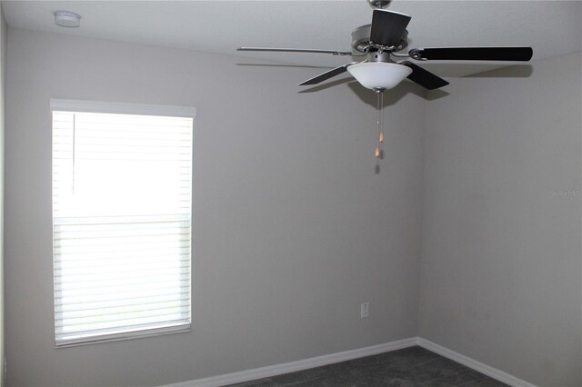 unfurnished room featuring ceiling fan, baseboards, dark carpet, and a wealth of natural light