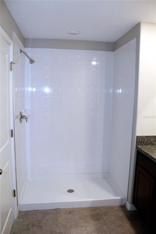 bathroom with a textured ceiling, tiled shower, and vanity