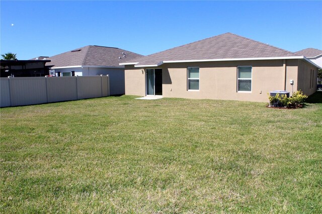 rear view of house featuring roof with shingles, stucco siding, central air condition unit, a lawn, and fence