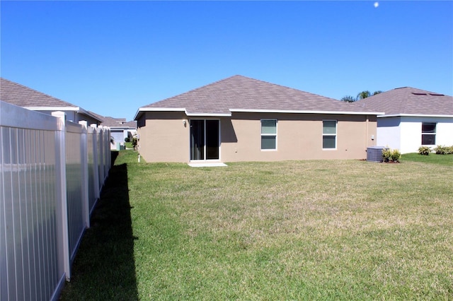 rear view of house featuring central air condition unit, a shingled roof, fence, a lawn, and stucco siding