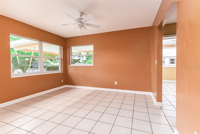 empty room featuring light tile patterned floors, plenty of natural light, a ceiling fan, and baseboards