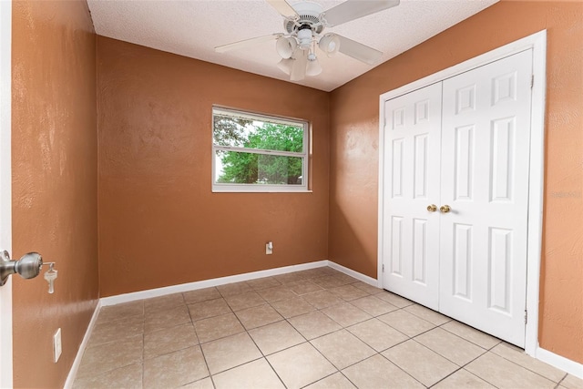 unfurnished bedroom with light tile patterned floors, a textured ceiling, a ceiling fan, baseboards, and a closet