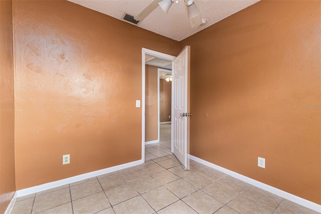 empty room featuring a textured ceiling, a textured wall, visible vents, and baseboards