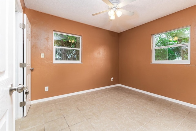 empty room featuring a wealth of natural light, ceiling fan, a textured ceiling, and baseboards