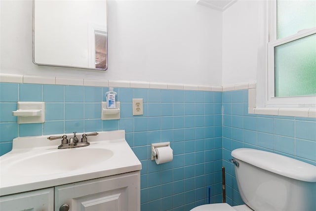 half bath featuring wainscoting, vanity, toilet, and tile walls