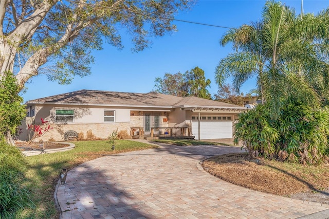 ranch-style house with an attached garage, stucco siding, a front lawn, french doors, and decorative driveway