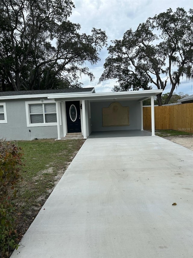 view of front facade with an attached carport, concrete driveway, fence, and stucco siding