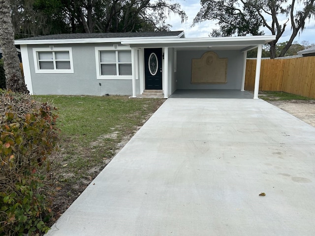 ranch-style house featuring stucco siding, a front lawn, fence, concrete driveway, and a carport