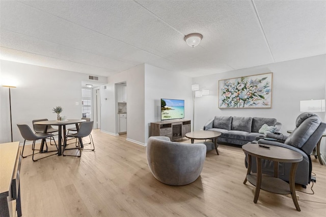 living room featuring light wood-type flooring, baseboards, a textured ceiling, and visible vents