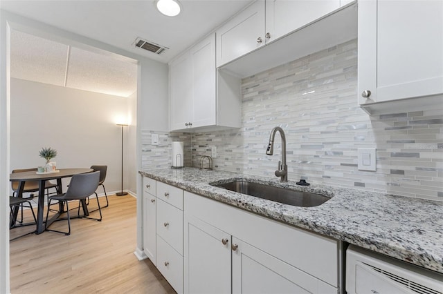 kitchen with visible vents, dishwasher, light wood-style floors, white cabinetry, and a sink