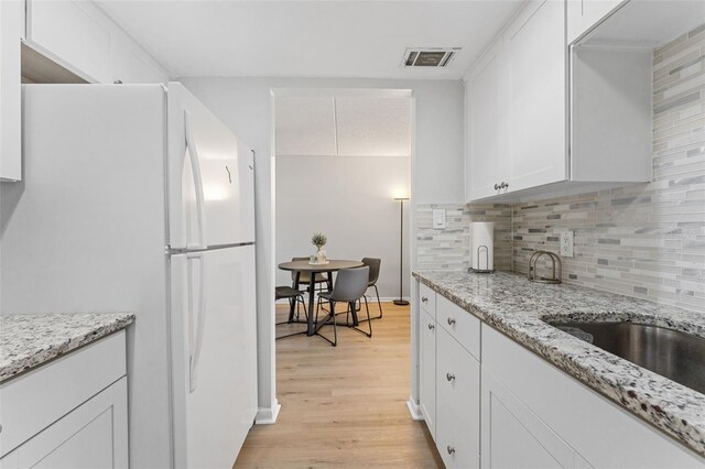 kitchen with visible vents, freestanding refrigerator, light wood-style floors, white cabinetry, and tasteful backsplash