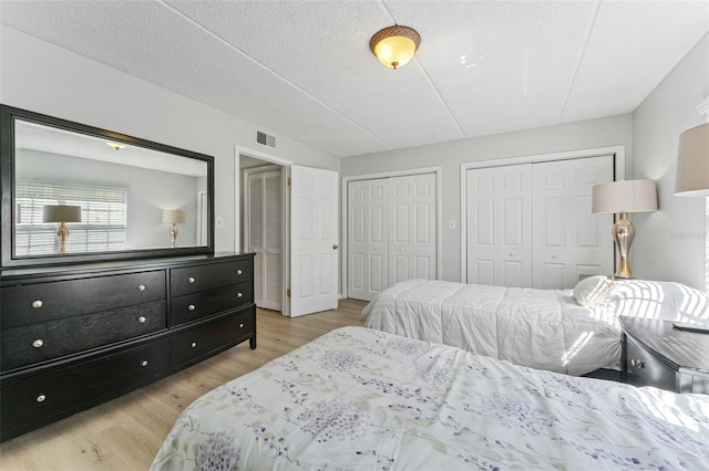 bedroom with visible vents, a textured ceiling, two closets, and light wood-style floors