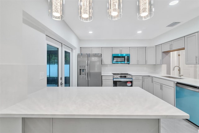 kitchen featuring appliances with stainless steel finishes, gray cabinets, a sink, and a peninsula