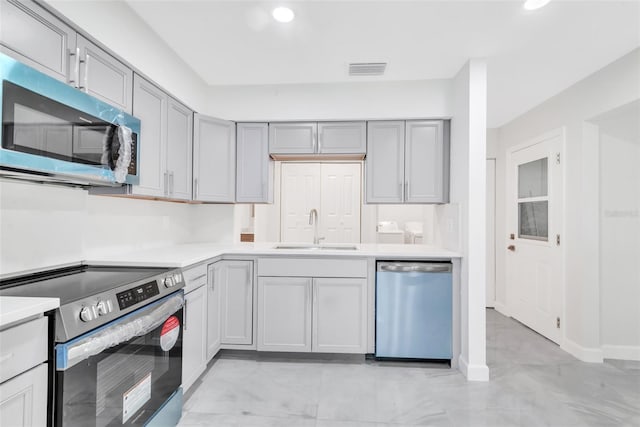 kitchen with stainless steel appliances, light countertops, a sink, and gray cabinetry