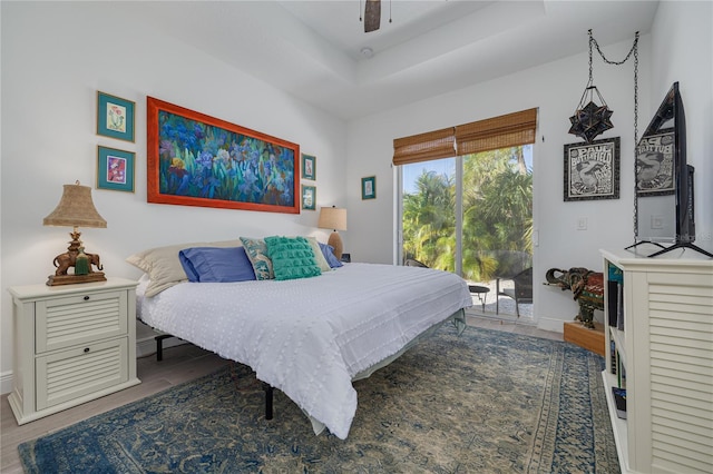 bedroom featuring ceiling fan, baseboards, wood finished floors, a raised ceiling, and access to outside