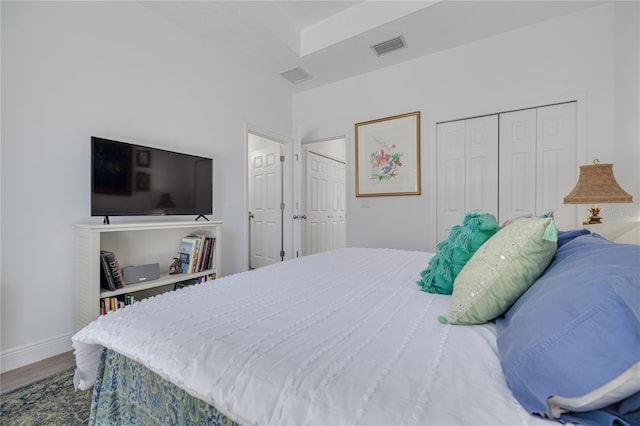 bedroom featuring visible vents, multiple closets, baseboards, and wood finished floors