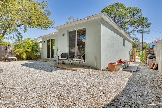 rear view of property with a patio area, fence, and stucco siding