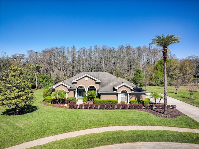 view of front of home featuring stucco siding, driveway, a forest view, and a front lawn