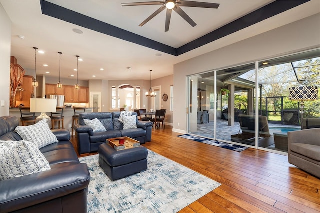 living room featuring baseboards, light wood-type flooring, recessed lighting, ceiling fan with notable chandelier, and arched walkways