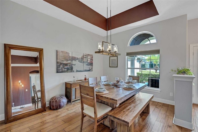 dining area featuring a chandelier, a raised ceiling, light wood-type flooring, and baseboards