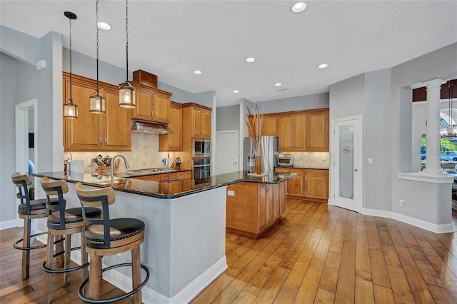 kitchen with under cabinet range hood, a peninsula, brown cabinets, and appliances with stainless steel finishes