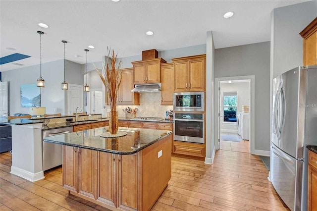 kitchen with under cabinet range hood, a sink, backsplash, stainless steel appliances, and a peninsula