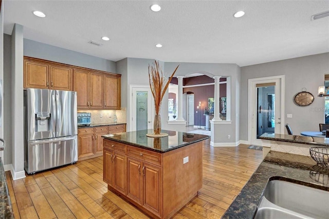 kitchen featuring arched walkways, stainless steel fridge, light wood-type flooring, and decorative columns