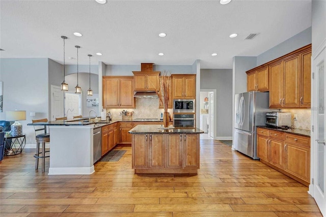 kitchen with visible vents, brown cabinets, a peninsula, stainless steel appliances, and a sink