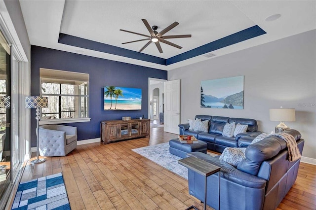 living room featuring hardwood / wood-style floors, a ceiling fan, baseboards, visible vents, and a raised ceiling