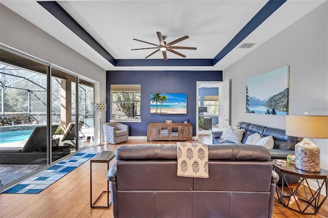 living room featuring plenty of natural light, visible vents, a tray ceiling, and a ceiling fan