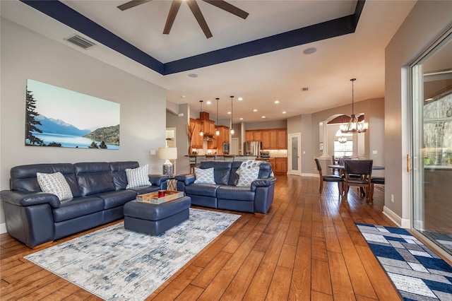 living room with hardwood / wood-style floors, visible vents, baseboards, recessed lighting, and ceiling fan with notable chandelier