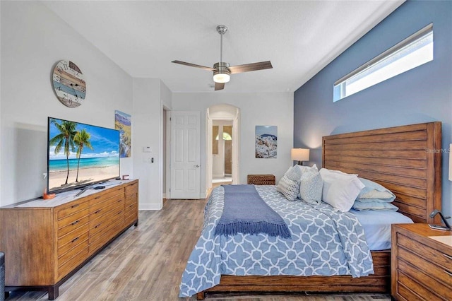 bedroom with connected bathroom, arched walkways, light wood finished floors, baseboards, and ceiling fan