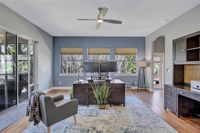 office space with light wood-type flooring, arched walkways, baseboards, and ceiling fan