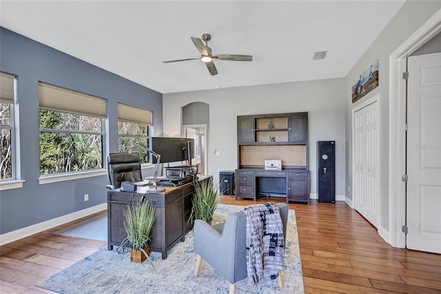 home office with a ceiling fan, baseboards, visible vents, arched walkways, and hardwood / wood-style flooring