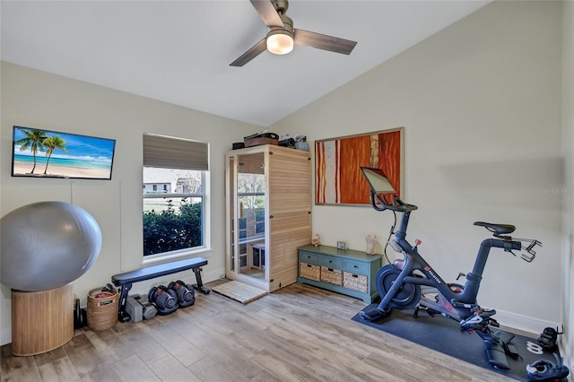 exercise area featuring ceiling fan, baseboards, light wood-style floors, and vaulted ceiling